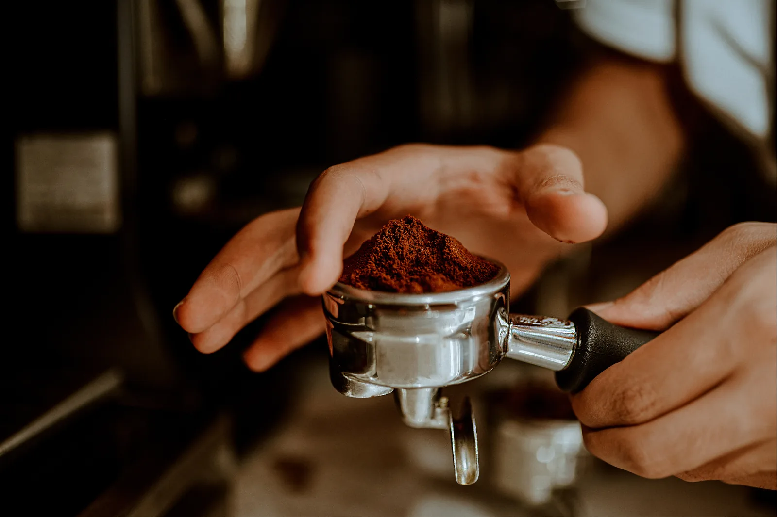 Portafiltre rempli de café fraîchement moulu, geste précis du barista avant tassage et extraction.