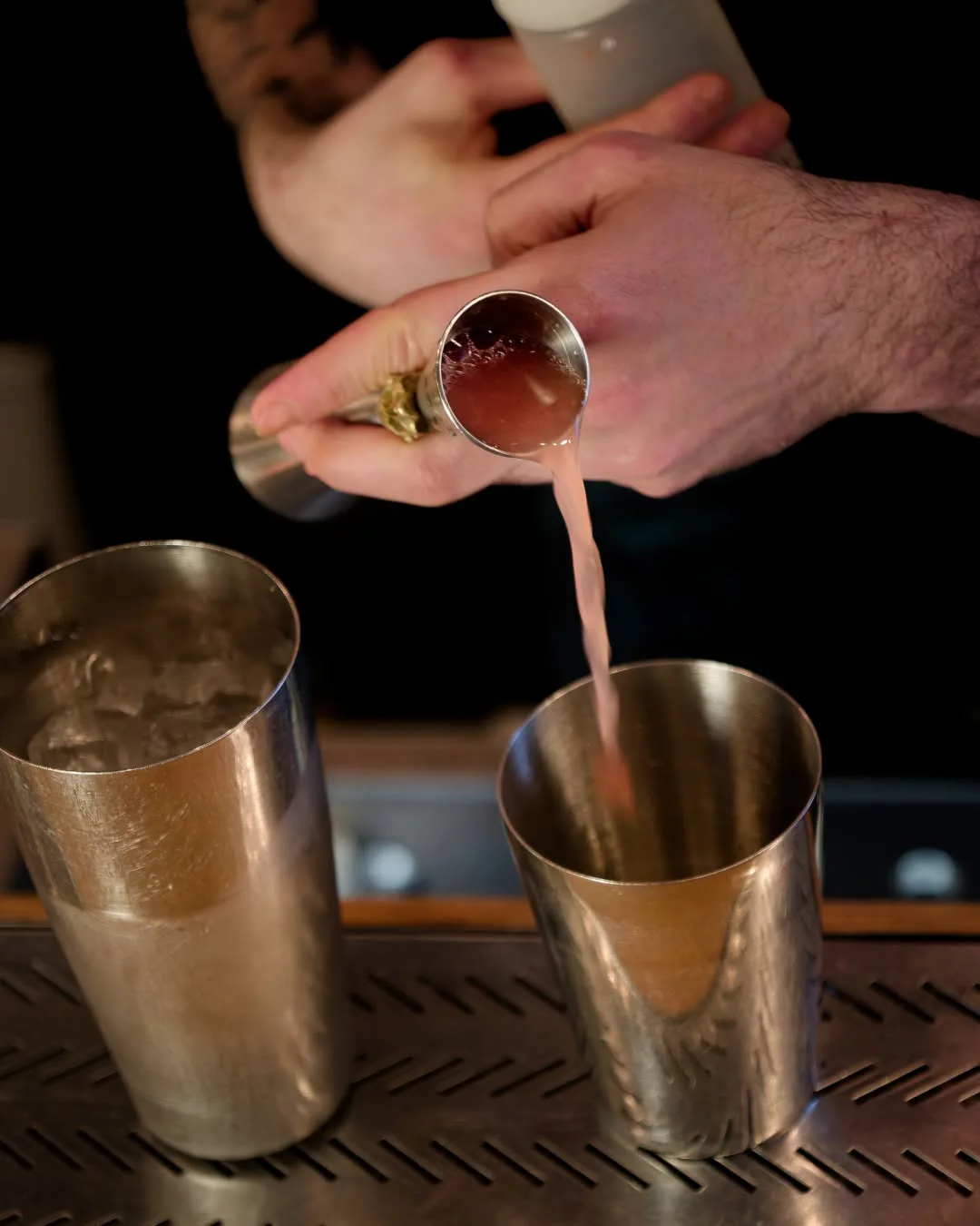 Bartender de The Modern Alchemist versant un cocktail au rhum à l'aide d'un jigger doré dans un shaker métallique.