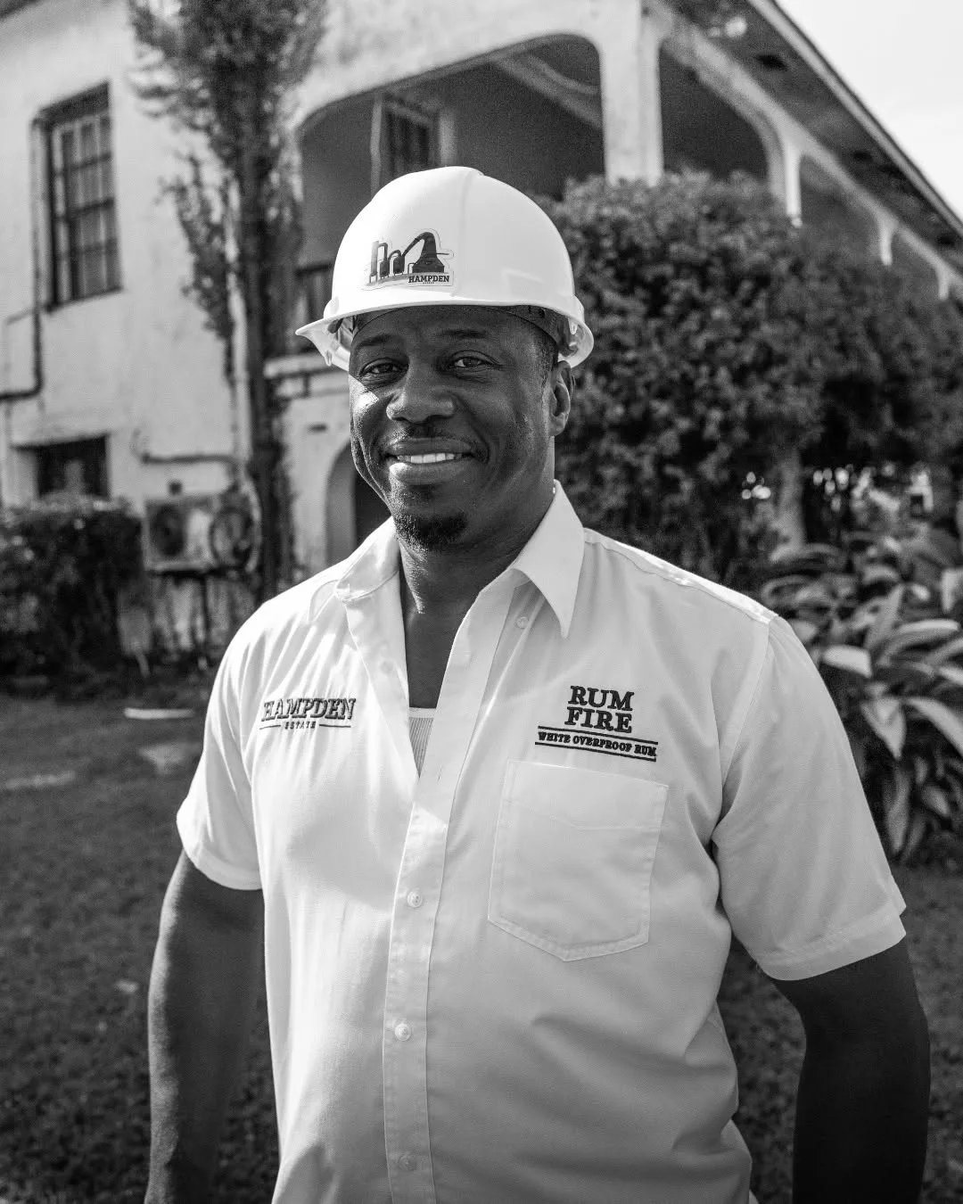 Portrait noir et blanc de Peppie Grant, Tour Manager chez Hampden Estate, devant la distillerie en Jamaïque.