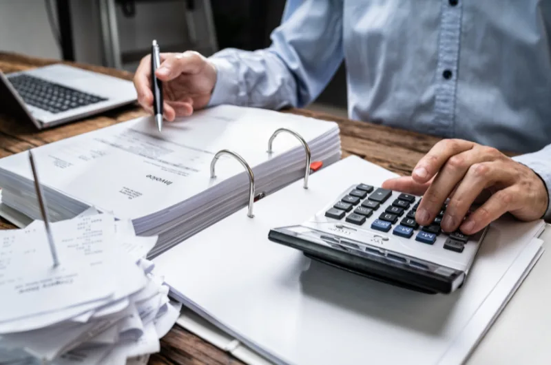 Restaurateur calculant ses marges sur une calculatrice, devant un classeur de factures.